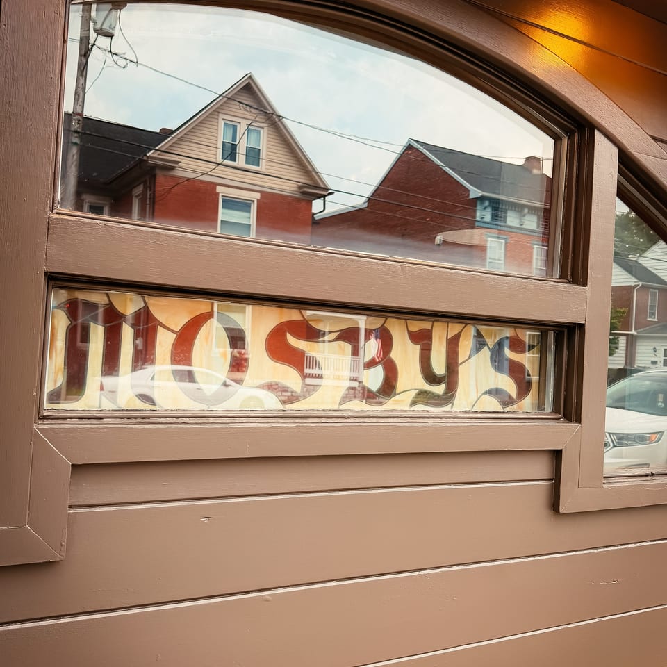 Brown wooden restaurant door with stained-glass panels, reflecting neighboring brick houses and a parked car.