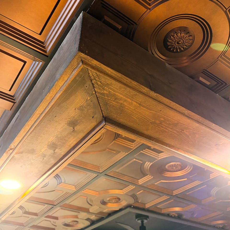 Ornate restaurant interior featuring geometric embossed ceiling panels, a decorative floral medallion, wood trim, and blue accent lighting.