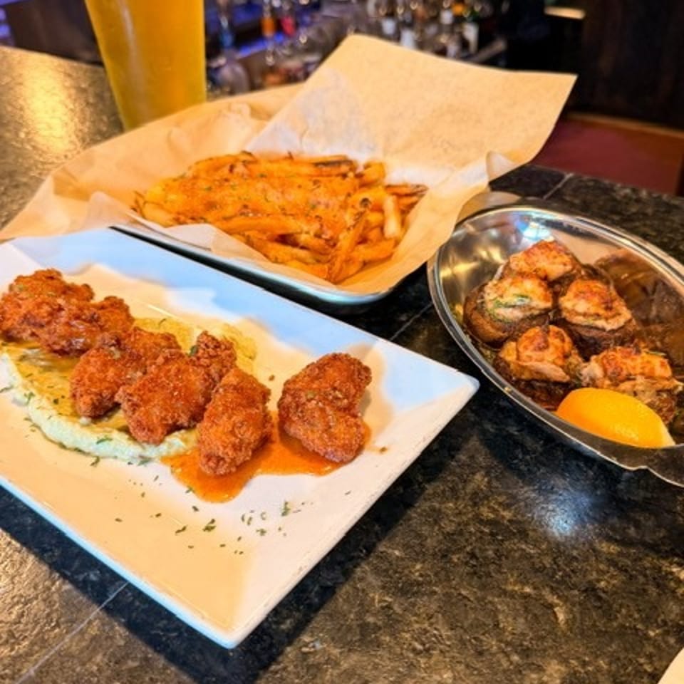 Bar counter displaying a pint of beer, crispy fried dishes, fries, and grilled bites with lemon.