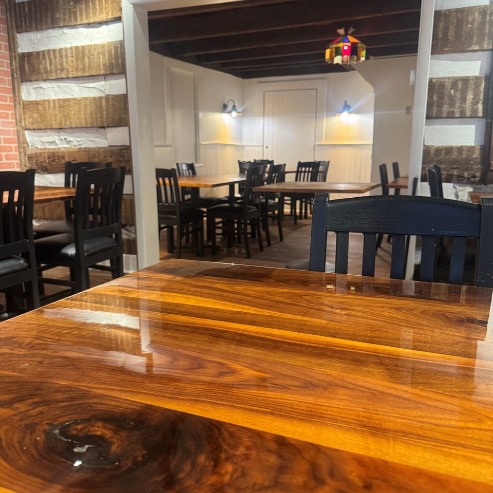 Rustic restaurant dining room with polished wooden tables, black chairs, exposed timber walls, and warm pendant lighting.